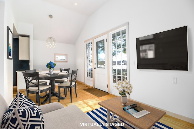 living area featuring light wood-type flooring, baseboards, vaulted ceiling, and a notable chandelier