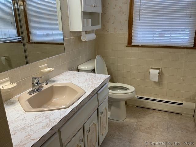 bathroom with tile walls, vanity, tile patterned flooring, toilet, and baseboard heating