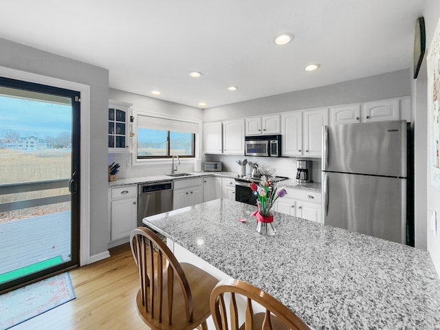 kitchen with a kitchen bar, stainless steel appliances, a sink, light stone counters, and glass insert cabinets