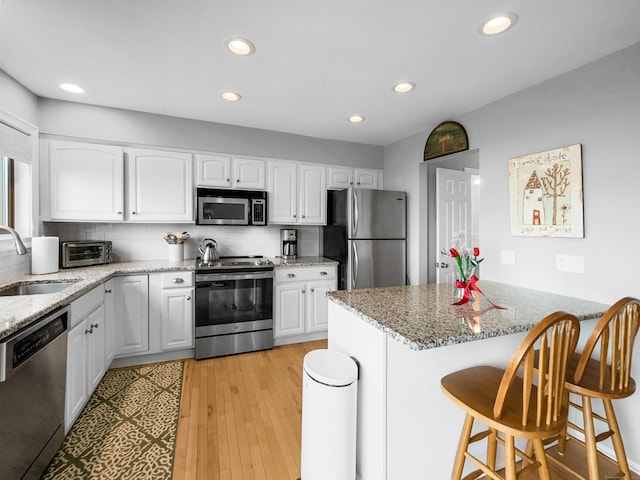 kitchen featuring white cabinetry, a sink, stainless steel appliances, and a breakfast bar area