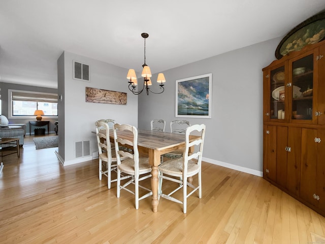 dining area with light wood finished floors, baseboards, visible vents, and a chandelier