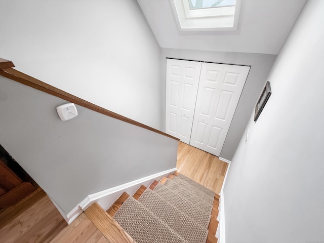 stairs with baseboards, wood finished floors, and lofted ceiling with skylight