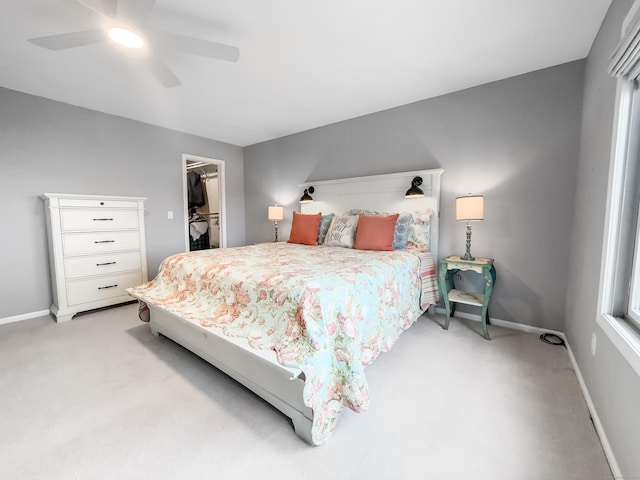 bedroom with light carpet, a closet, ceiling fan, and a spacious closet