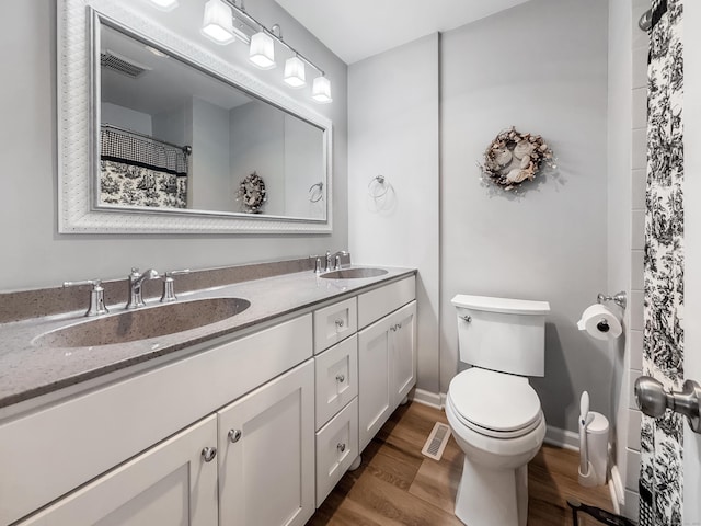 bathroom featuring toilet, a sink, wood finished floors, and visible vents