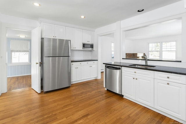 kitchen with dark countertops, appliances with stainless steel finishes, white cabinets, a sink, and light wood-type flooring