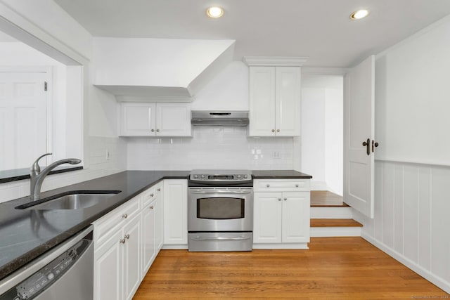 kitchen with appliances with stainless steel finishes, dark countertops, a sink, and white cabinetry