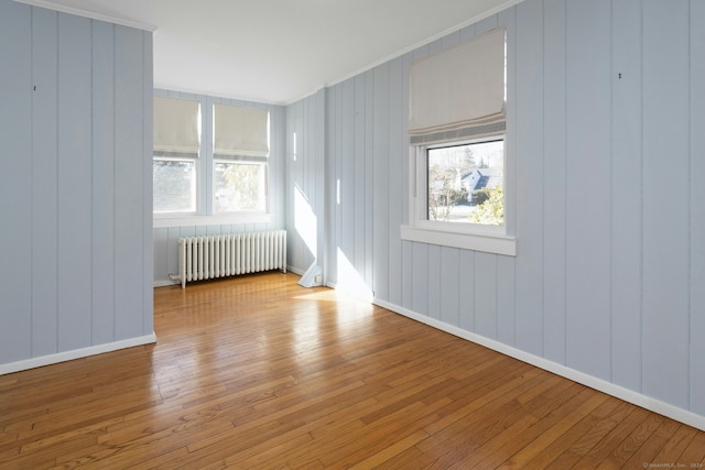 empty room with radiator, light wood-style floors, baseboards, and a wealth of natural light