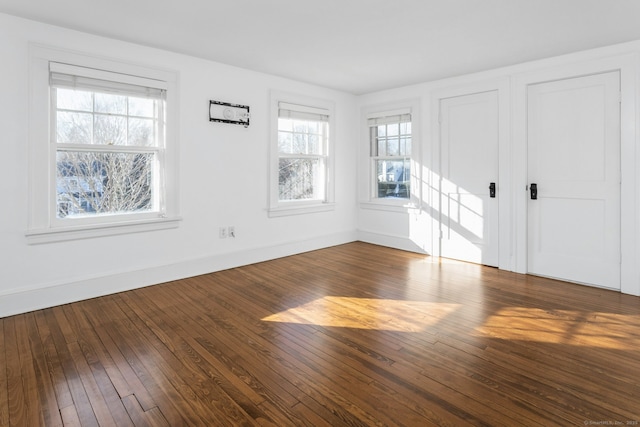 spare room featuring plenty of natural light, baseboards, and dark wood-type flooring