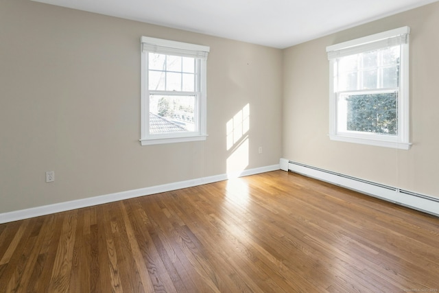 empty room with baseboard heating, wood finished floors, and baseboards