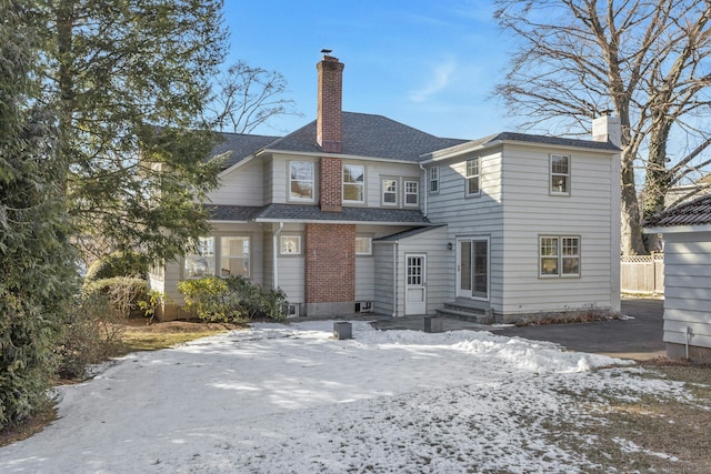 snow covered house featuring roof with shingles and a chimney