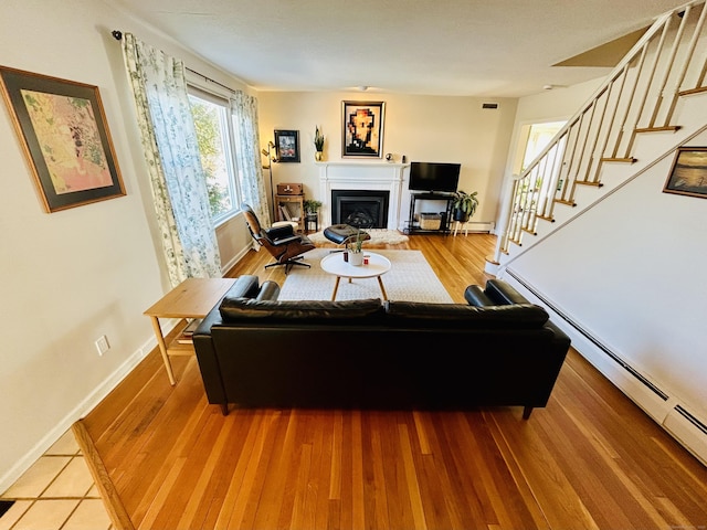 living area featuring baseboards, a baseboard radiator, stairway, light wood-type flooring, and a fireplace