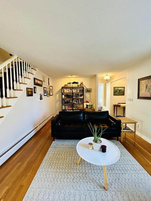 living room with a textured ceiling, stairway, baseboard heating, and wood finished floors