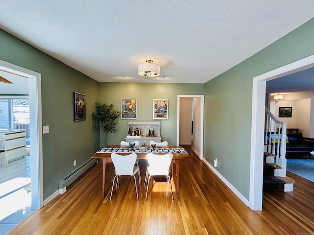 dining space featuring hardwood / wood-style flooring, a baseboard radiator, stairway, and baseboards