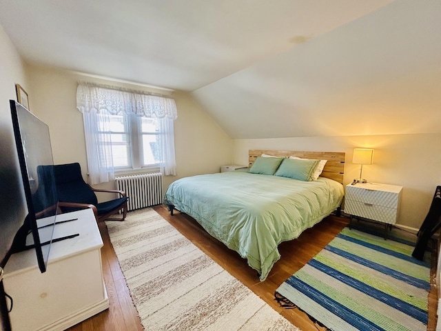 bedroom featuring lofted ceiling, radiator, and wood finished floors