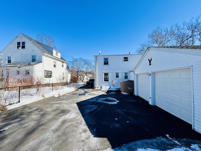 snow covered back of property with a garage, an outbuilding, fence, and cooling unit