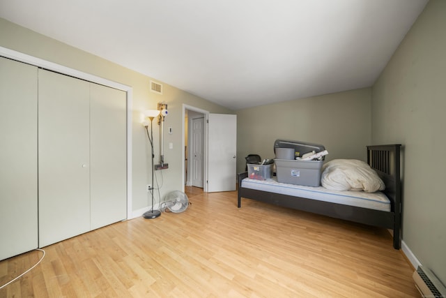 bedroom with light wood-type flooring, baseboard heating, and a closet