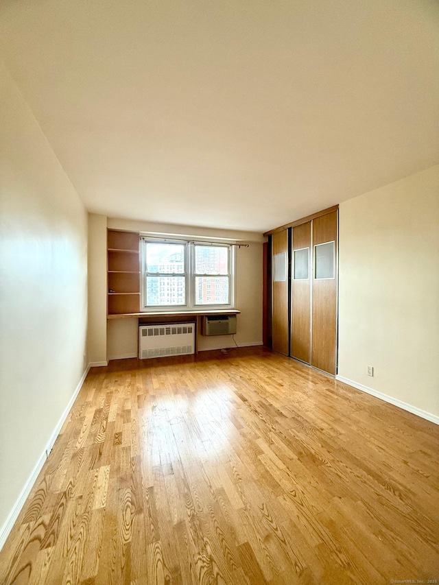 unfurnished bedroom featuring radiator heating unit, light hardwood / wood-style floors, and an AC wall unit