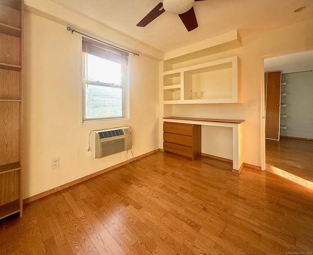 unfurnished living room featuring ceiling fan, a wall mounted AC, built in desk, and wood-type flooring