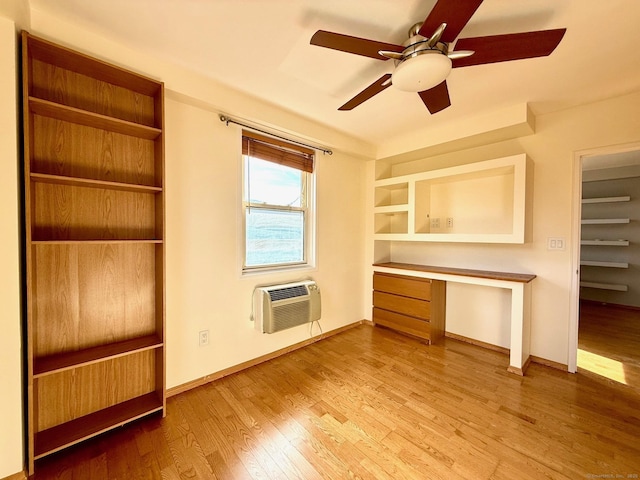 interior space featuring hardwood / wood-style flooring, built in shelves, a wall unit AC, ceiling fan, and built in desk