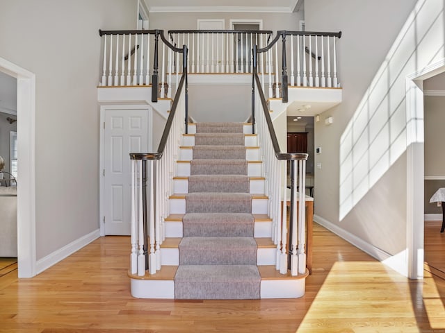 stairs with ornamental molding, a towering ceiling, baseboards, and wood finished floors