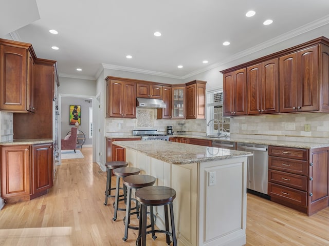 kitchen with range, light wood-style floors, under cabinet range hood, a kitchen bar, and stainless steel dishwasher