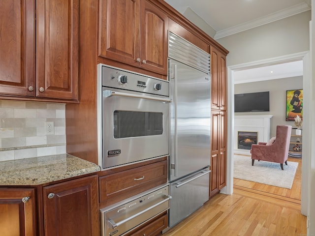 kitchen with light stone counters, a warming drawer, crown molding, stainless steel appliances, and backsplash