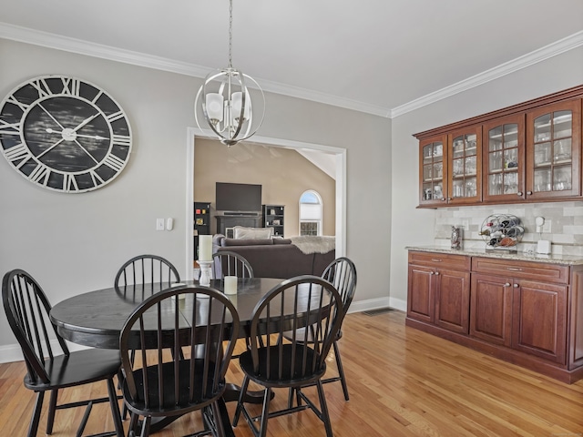 dining space featuring light wood-type flooring, an inviting chandelier, baseboards, and ornamental molding