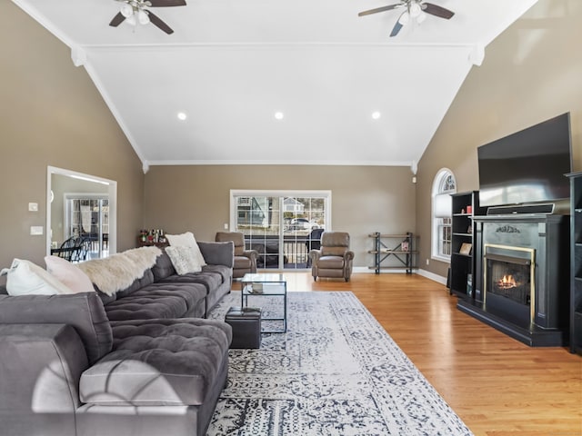 living room with a warm lit fireplace, ceiling fan, baseboards, and wood finished floors