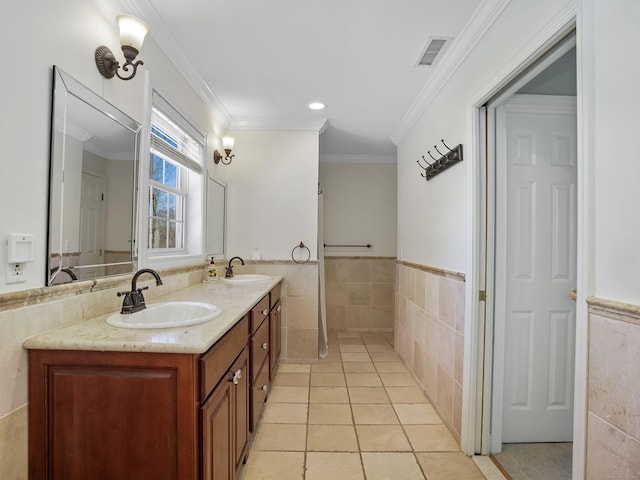 full bath with a wainscoted wall, visible vents, tile walls, and a sink