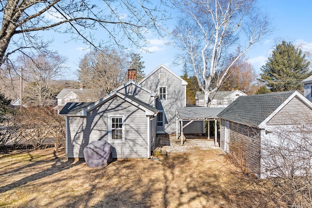 rear view of house with driveway, a chimney, and a lawn