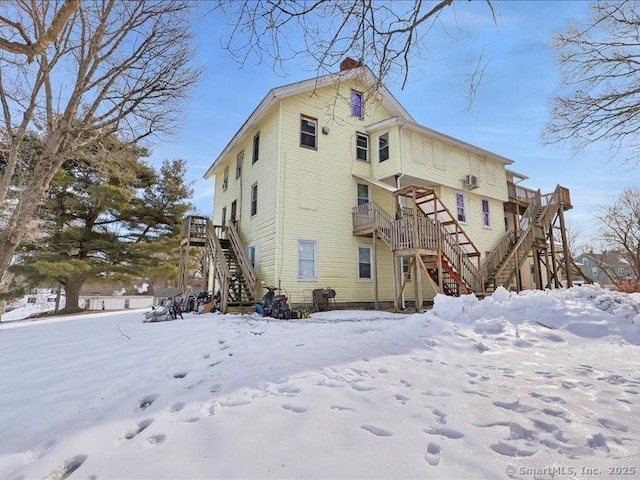 snow covered rear of property featuring a chimney and stairs