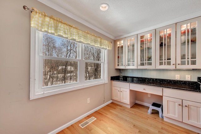 unfurnished office with a textured ceiling, visible vents, baseboards, light wood-type flooring, and built in study area