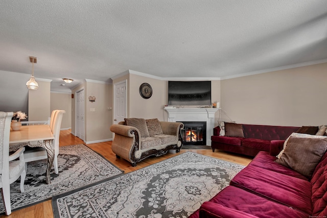 living area featuring a textured ceiling, light wood-style flooring, baseboards, ornamental molding, and a glass covered fireplace