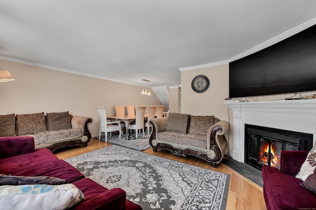 living area with ornamental molding, a glass covered fireplace, a textured ceiling, and wood finished floors