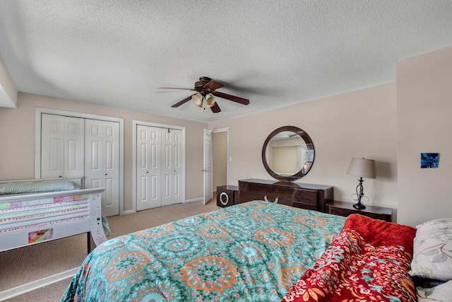 bedroom with ceiling fan, a textured ceiling, two closets, and light colored carpet