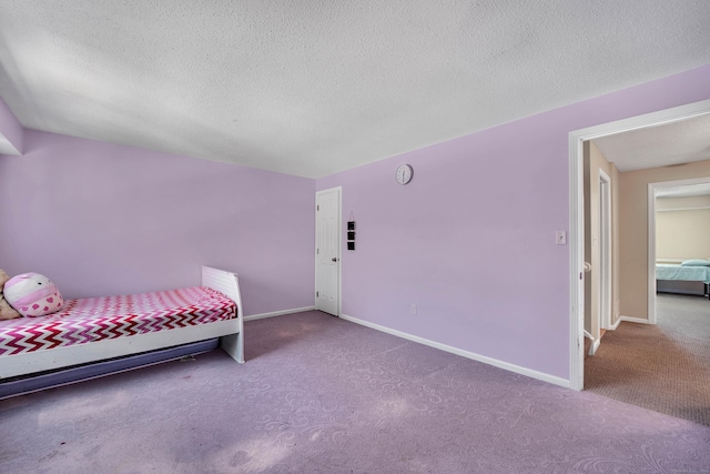 unfurnished bedroom with a textured ceiling, carpet flooring, and baseboards