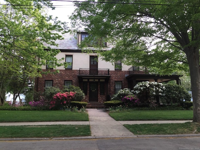 tudor home with brick siding, a front lawn, and stucco siding