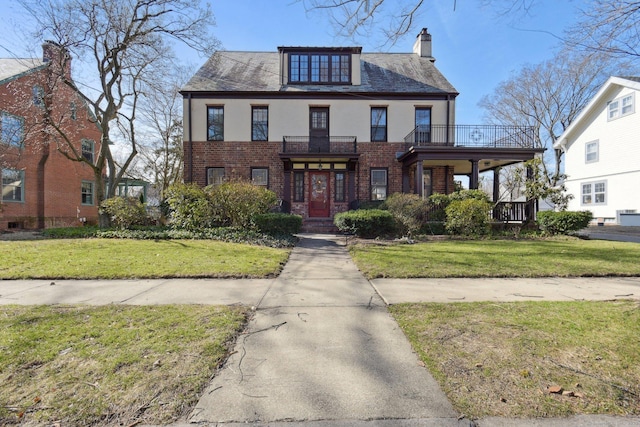 view of front of property featuring a front lawn, a balcony, brick siding, and stucco siding