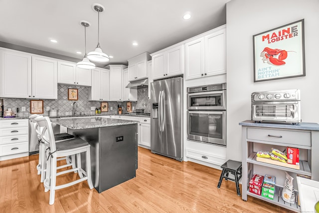 kitchen with white cabinetry, stainless steel appliances, light stone counters, and decorative light fixtures