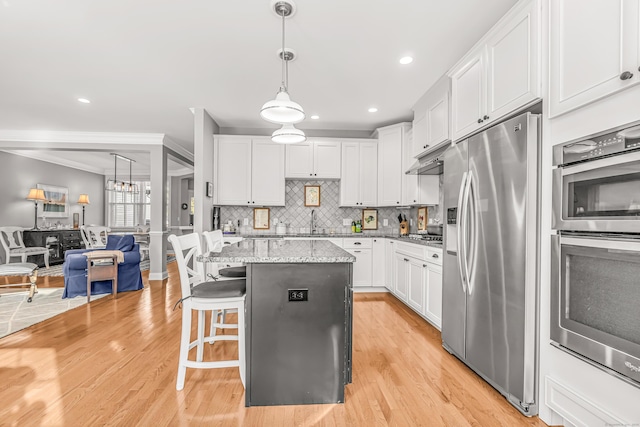 kitchen with hanging light fixtures, a kitchen island, light stone countertops, appliances with stainless steel finishes, and white cabinets