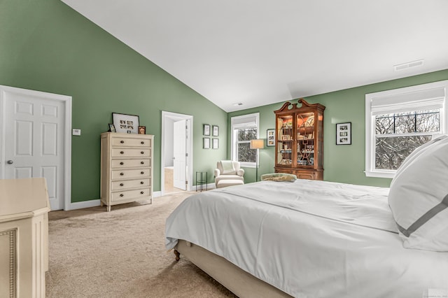 bedroom with light carpet, ensuite bathroom, and vaulted ceiling