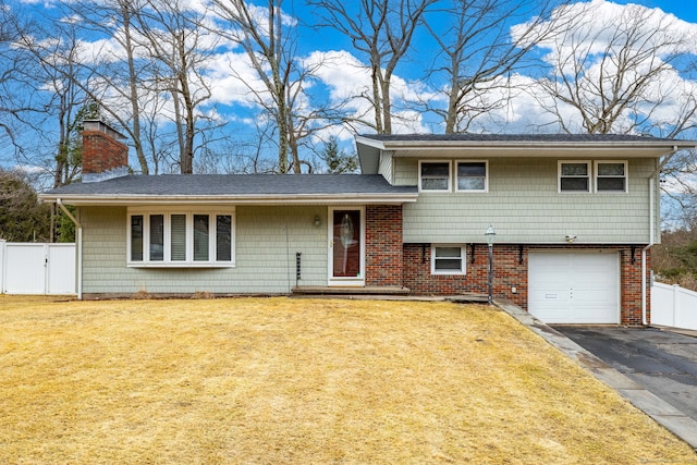 split level home with brick siding, fence, driveway, a chimney, and a front yard