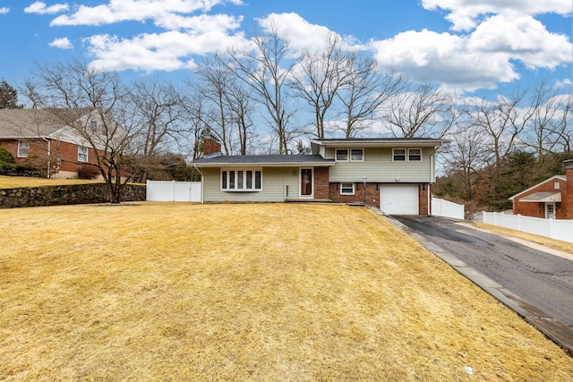 view of front of home with aphalt driveway, brick siding, fence, a front lawn, and a chimney