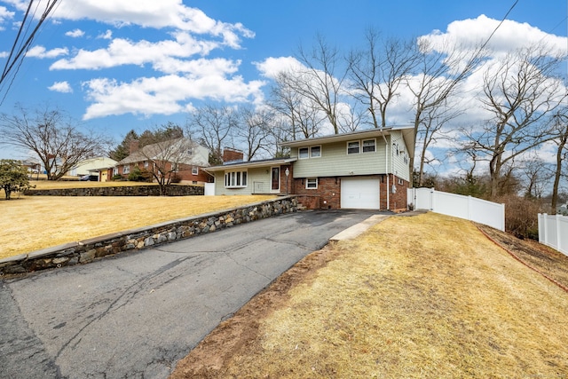 view of front of home with aphalt driveway, brick siding, fence, a garage, and a front lawn