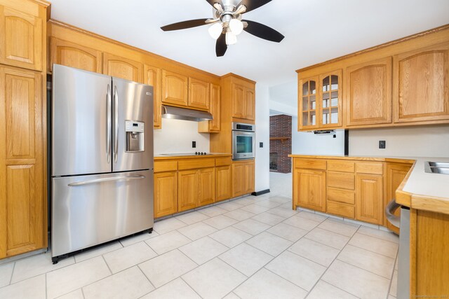 kitchen featuring a ceiling fan, glass insert cabinets, appliances with stainless steel finishes, light countertops, and under cabinet range hood