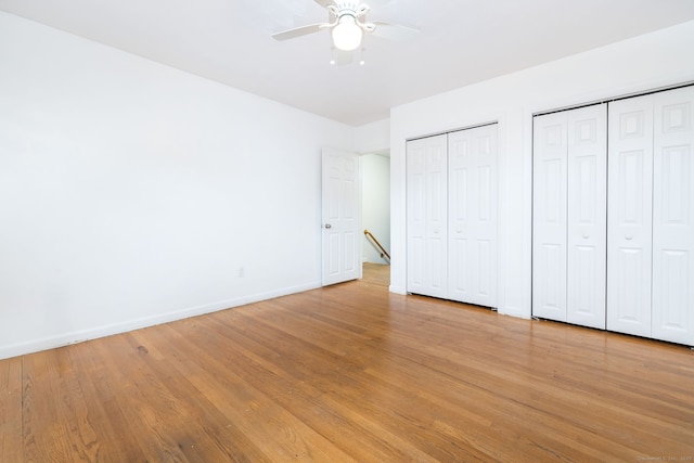 unfurnished bedroom featuring baseboards, ceiling fan, light wood-style floors, and multiple closets