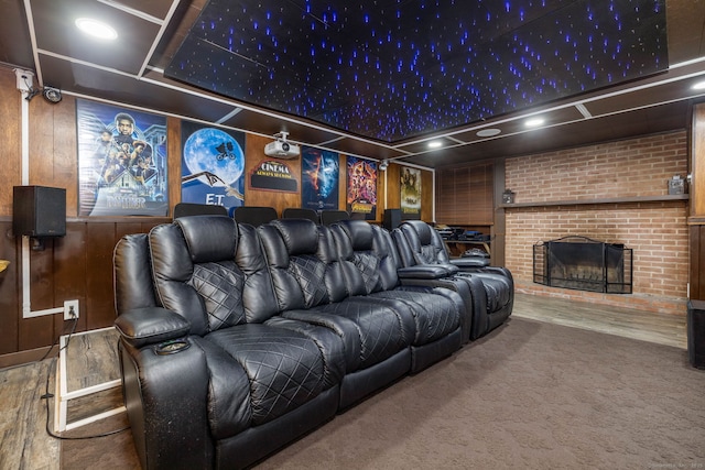 carpeted cinema room with a brick fireplace, wooden walls, and wood finished floors