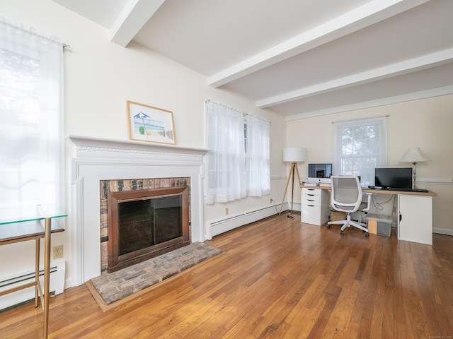 office space featuring wood-type flooring, a baseboard heating unit, beam ceiling, and a glass covered fireplace