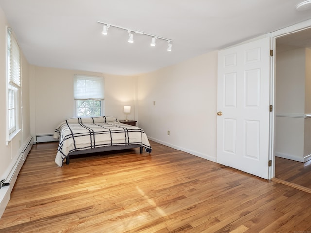 bedroom with light wood finished floors, a baseboard radiator, and baseboards