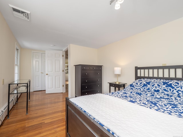 bedroom featuring a baseboard heating unit, a closet, visible vents, and wood finished floors